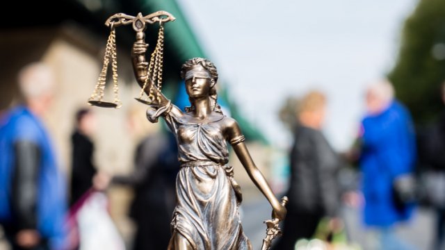 Statue der Justitia, der Göttin der Gerechtigkeit. Eine Menschenmenge im Hintergrund.